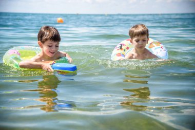 Mutlu çocuklar sahilde sörf yaparken eğleniyor. Şen şakrak bir çift çocuk kırılma dalgasında şişirilebilir ring gezintisinde. Seyahat yaşam tarzı, aile yaz kampında yüzme aktiviteleri. Tropikal adada tatiller.