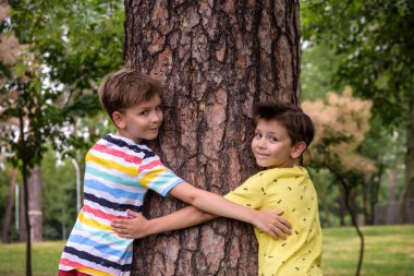 İki küçük çocuk bir ağaç gövdesine sarılıyor - çocuklar doğayı seviyor, sürdürülebilirlik kavramını. Doğayı kurtar..