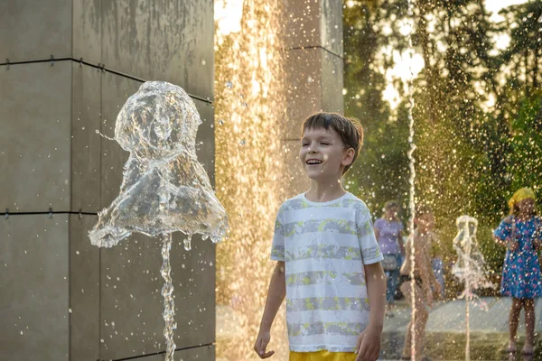 Boy having fun in water fountains. Child playing with a city fountain on hot summer day. Happy kids having fun in fountain. Summer weather. Active leisure, lifestyle and vacation.