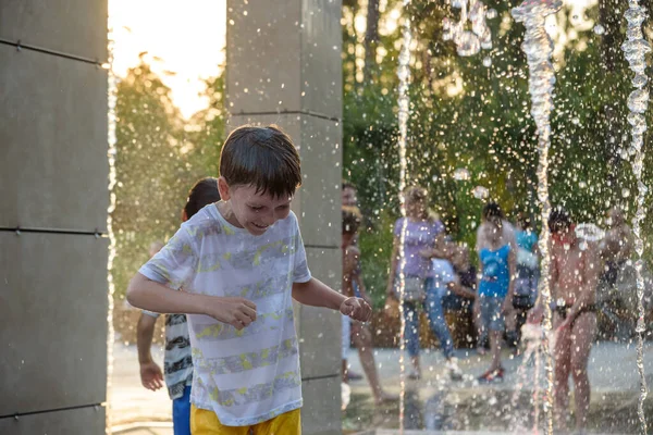 Boys jumping in water fountains. Children playing with a city fountain on hot summer day. Happy friends having fun in fountain. Summer weather. Friendship, lifestyle and vacation.