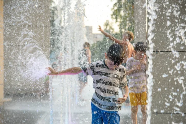 Boys jumping in water fountains. Children playing with a city fountain on hot summer day. Happy friends having fun in fountain. Summer weather. Friendship, lifestyle and vacation.