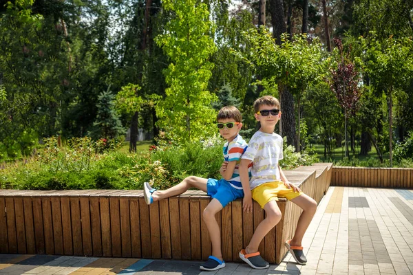 Gülümseyen çocukların şehir parkında vakit geçirmesi, çocuk ve kardeşinin bankta oturması... Mutlu çocukluk kavramı. Neşeli çocuklar doğada dinleniyor..