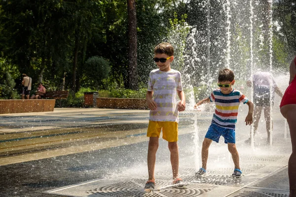 Boy having fun in water fountains. Child playing with a city fountain on hot summer day. Happy kids having fun in fountain. Summer weather. Active leisure, lifestyle and vacation.