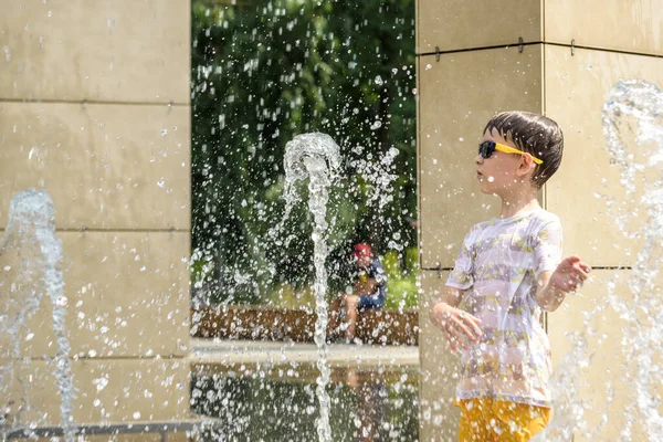 Boy having fun in water fountains. Child playing with a city fountain on hot summer day. Happy kids having fun in fountain. Summer weather. Active leisure, lifestyle and vacation.