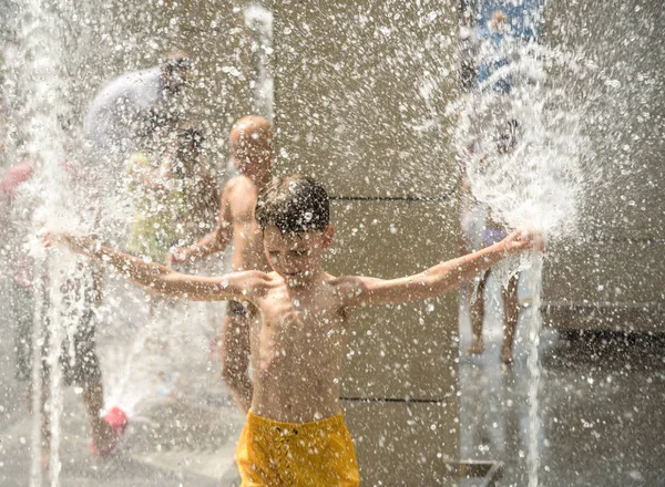 Boy having fun in water fountains. Child playing with a city fountain on hot summer day. Happy kids having fun in fountain. Summer weather. Active leisure, lifestyle and vacation.