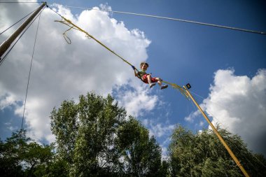 Çocuk bungee trambolinde zıplıyor. Sigortası ve esneyebilir lastikleri olan bir çocuk gökyüzüne asılı duruyor. Eğlence parkında mutlu çocukluk ve oyun kavramı.