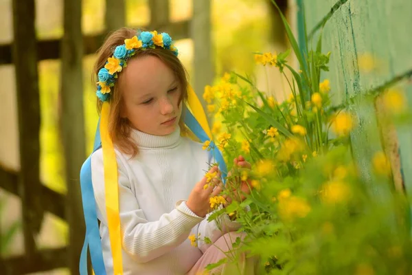 Una niña en una corona de flores en un prado verde en una chaqueta blanca en primavera y verano —  Fotos de Stock