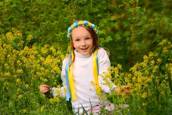 Una ragazza in una ghirlanda di fiori in un prato verde in una giacca bianca in primavera ed estate — Foto Stock