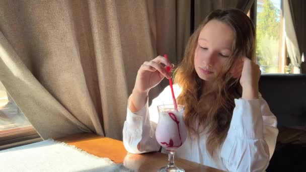 Ένα κορίτσι πίνει ένα ροζ κοκτέιλ από ένα κόκκινο καλαμάκι σε ένα εστιατόριο — Αρχείο Βίντεο