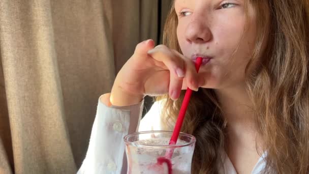 Девушка пьет розовый коктейль из красной трубочки в ресторане — стоковое видео