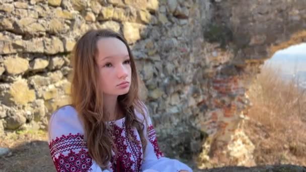 Pas de guerre jeune fille ukrainienne dans un chemisier brodé sur les ruines d'un vieux château triste et regarde tout autour — Video