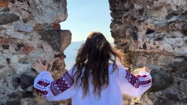 Pas de guerre jeune fille ukrainienne dans un chemisier brodé sur les ruines d'un vieux château triste et regarde tout autour — Video