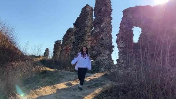 Pas de guerre jeune fille ukrainienne dans un chemisier brodé sur les ruines d'un vieux château triste et regarde tout autour — Video