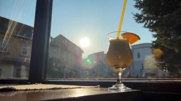 Χυμό ακτινίδιο και ποτό πορτοκάλι Kilimonjaro στο φόντο του παραθύρου και τον λαμπερό ήλιο με ένα κομμάτι πορτοκάλι σε ένα ποτήρι — Αρχείο Βίντεο