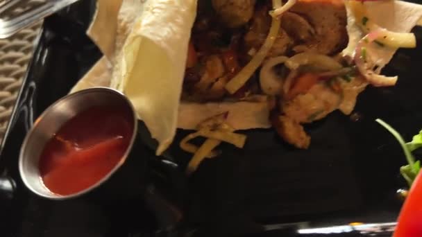 Kebab caldo su un piatto nero in un ristorante con lattuga e bistecca di pomodori si trova su un pane pita sottile e sembra molto appetitoso — Video Stock