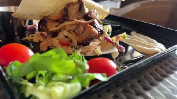 Kebab chaud sur une assiette noire dans un restaurant avec de la laitue et des tomates steak repose sur un pain pita mince et semble très appétissant — Video