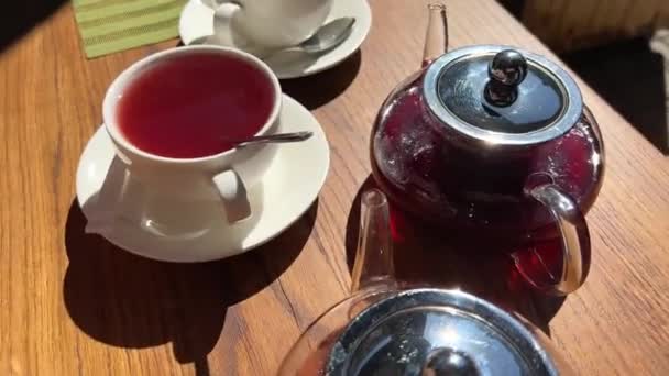 Varm tranbär och vinbär te två tekannor står på ett träbord från dem hälls i en vit kopp ångande dryck — Stockvideo