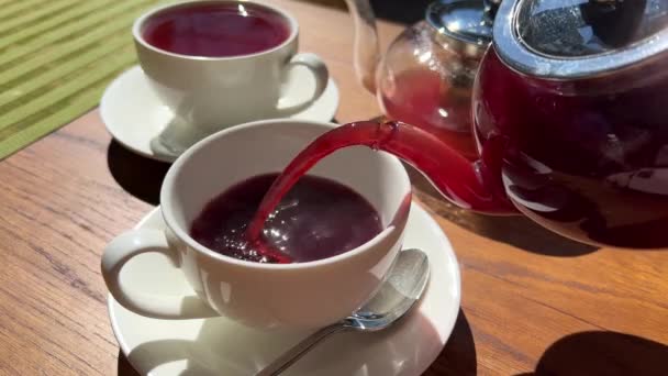 Forró áfonya és ribizli tea két teáskanna áll egy fából készült asztalon, amit egy fehér csésze gőzölgő italba öntöttek. — Stock videók
