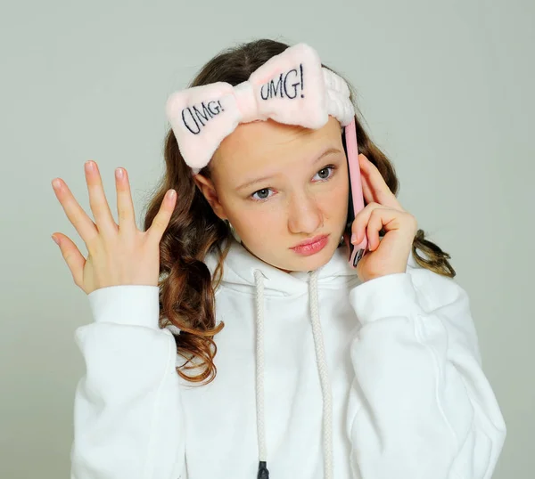 Teenager Mädchen in einem weißen Kapuzenpullover im Studio auf weißem Hintergrund verschiedene Fratzen, sie ist jung, sie hat ein Handy in der Hand, macht ein Selfie und bewundert sich selbst und einen rosa Verband — Stockfoto