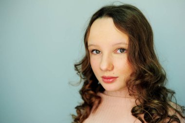 Makyaj stüdyosundaki pembe golflü bir kız gözlerinde yeni bir makyajla mutlu bir şekilde gülümser. Fotoğrafçılık için bir lamba yansıtır. Nazikçe kirpiklerini boyarlar ve dudakları sarı saçlı 10-13 yaşlarında bir kız.