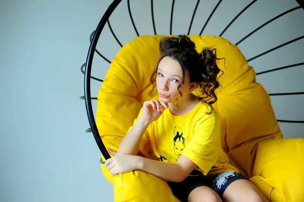 摇椅一个穿着鲜艳黄色运动衫的女孩坐在一张多汁的黄色椅子上，面对着不同的情绪，在工作室的白色背景下，她正开心地微笑着 — 图库照片