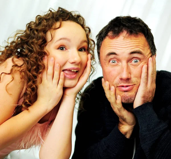 女孩和父亲站在不同的惊讶的面孔上玩耍。 12岁的女孩和大约40岁的父亲在演播室里，背景是白色的 — 图库照片