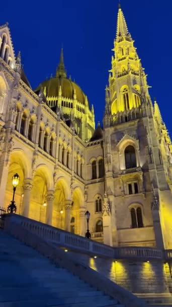Edificio del Parlamento húngaro en Budapest fotografía nocturna de paredes iluminadas de color amarillo brillante y cielo azul oscuro cerca del río Danubio 03.04.22 Budapest, Hungría — Vídeos de Stock