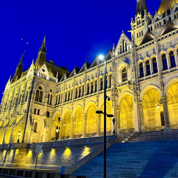 Edificio del Parlamento húngaro en Budapest fotografía nocturna de paredes iluminadas de color amarillo brillante y cielo azul oscuro cerca del río Danubio 03.04.22 Budapest, Hungría — Foto de Stock