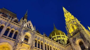 Budapeşte 'deki Macar Parlamentosu binası. Parlak sarı ışıklı duvarlar ve Tuna Nehri yakınlarındaki koyu mavi gökyüzü. 03.04.22 Budapeşte, Macaristan