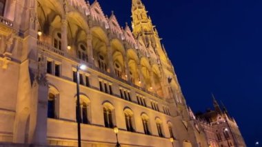 Budapeşte 'deki Macar Parlamentosu binası. Parlak sarı ışıklı duvarlar ve Tuna Nehri yakınlarındaki koyu mavi gökyüzü. 03.04.22 Budapeşte, Macaristan