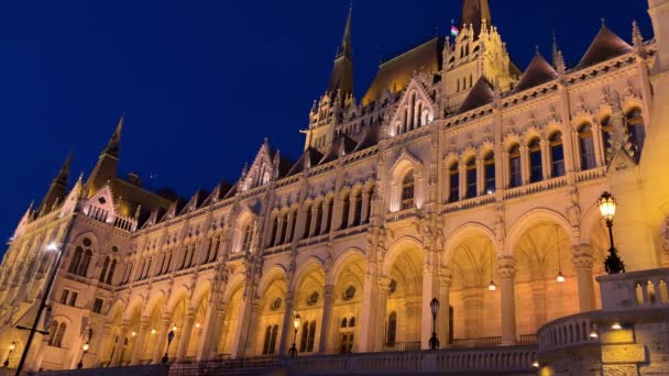 Budova maďarského parlamentu v Budapešti v noci fotografie jasně žlutých osvětlených stěn a tmavě modré oblohy u Dunaje 03.04.22 Budapešť, Maďarsko — Stock video