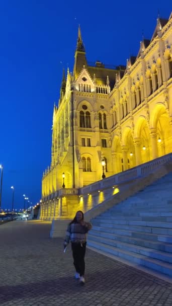 Węgierski budynek parlamentu w Budapeszcie nocą fotografii jasnożółtych podświetlanych ścian i ciemnoniebieskiego nieba w pobliżu Dunaju 03.04.22 Budapeszt, Węgry — Wideo stockowe