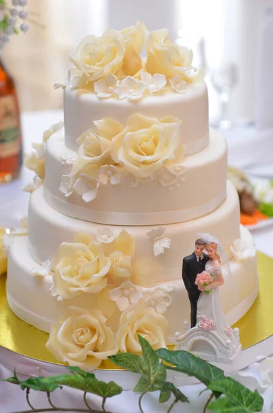 Wedding cake with white cream and beige pink roses with sculptures of the bride and groom on a gold stand — Stock Photo, Image