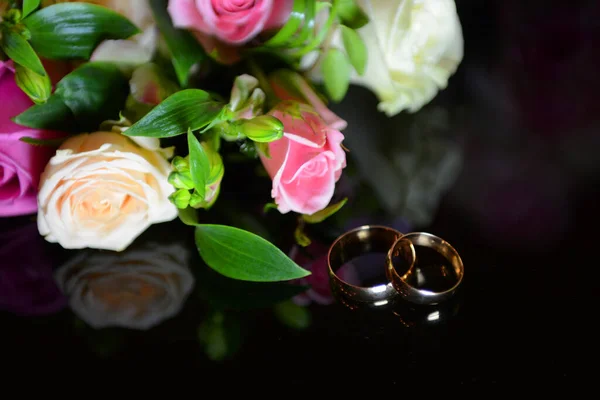 Hochzeitsstrauß mit goldenen Eheringen auf einem dunklen Tisch mit Spiegelung ein wunderbarer Hintergrund für Werbesalons — Stockfoto