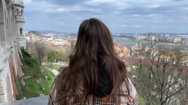 En flicka tittar från en höjd på staden Fishermans bastion attraktion av Buda slott vit sten fästning med sju torn med den vackraste utsikten över Donau och Pest — Stockvideo