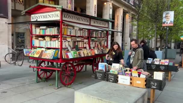 Red book stall on wheels on the street of Budapest and an elderly couple of a man and a woman who choose a book 06.04.22 Budapest Hungary — 비디오