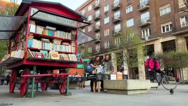 Rode boekenkraam op wielen in de straat van Boedapest en een ouder echtpaar van een man en een vrouw die voor een boek kiezen 06.04.22 Boedapest Hongarije — Stockvideo