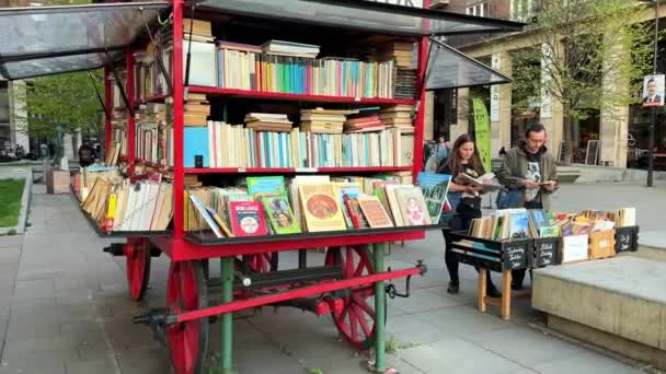 Rode boekenkraam op wielen in de straat van Boedapest en een ouder echtpaar van een man en een vrouw die voor een boek kiezen 06.04.22 Boedapest Hongarije — Stockvideo