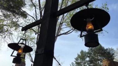 Gökyüzüne karşı eski bir lamba parlıyor ve ağaç dallanıyor ateş yanıyor ve arka planda eski bir taş ev var.