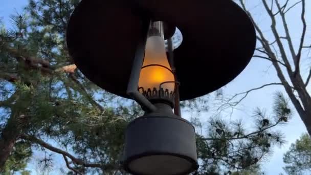 Een oude lamp gloeit tegen de hemel en takken het vuur brandt en op de achtergrond een oud stenen huis — Stockvideo