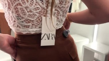 Mağazada genç bir kız tarafından giyilen beyaz önlük ve kahverengi pantolon. Soyunma odasında Zara. Güzel bir yakın çekim 06.04.22 Paris Fransa Zara mağazası.