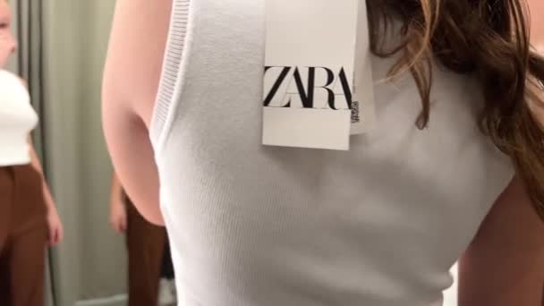 Braune Hose und weißes T-Shirt im Bekleidungsgeschäft Ein Mädchen in der Umkleidekabine misst Zara-Kleidung — Stockvideo