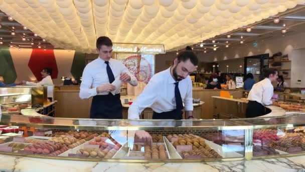 La vie dans la confiserie Makarunov Pierre Edme dans les vendeurs blancs agitation essayer de plaire aux acheteursBeaucoup de macarons et une fille en blanc choisit un goût 06.04.22 Paris France — Video