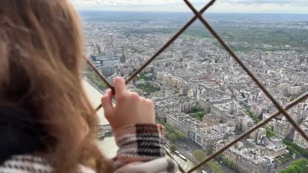 A girl on a eiffel tower looks around at the city of Paris visible houses the Seine River with boats and the city center 06.04.22 Paris France — Stock Video