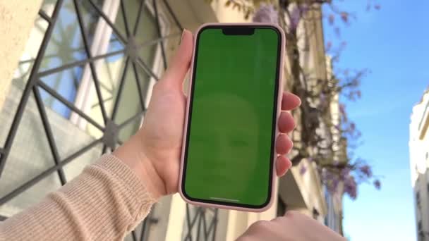 Una mano de mujer con vitiligo sostiene un smartphone con pantalla verde. Vista trasera. Tecla de croma, teléfono de mano de mujer de primer plano con pantalla verde vertical. — Vídeos de Stock
