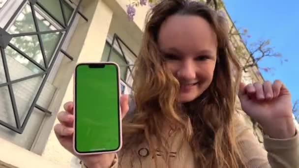 Teenage κορίτσι με χαλαρά μαλλιά καστανά μαλλιά χοροί με το τηλέφωνο χαίρεται στην οθόνη του χωλότητα πράσινο οθόνη μπεζ φόντο — Αρχείο Βίντεο