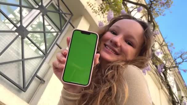The girl hugs the phone presses her cheek against it green screen and chromate in a pink case the girl smiles and shrugs her shoulder — стоковое видео
