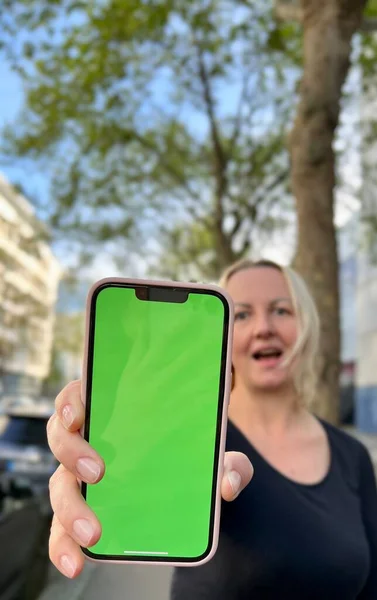 Adolescente aux cheveux lâches cheveux bruns danses de cheveux bruns avec téléphone se réjouit sur l'écran de boiterie écran vert fond beige — Photo