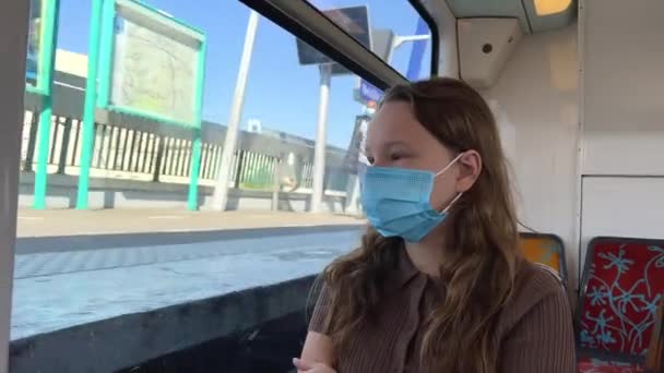 10代の女の子の茶色の髪は地下鉄の座ってマスクの茶色の服で細長いです彼女が離陸し、マスクを置くビデオがあります。電車の中を歩く。電話で緑色の画面が表示されます. — ストック動画