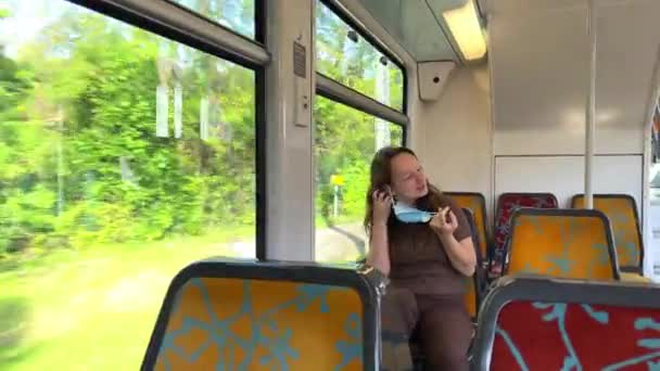 小女孩棕色的头发是纤细的，穿着棕色衣服，戴着地铁座位的面具。在视频中，她摘下并戴上了面具。走在火车上在电话上显示绿色屏幕跳舞和微笑. — 图库视频影像